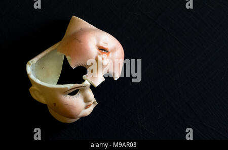 Broken doll face on black background. Conceptual image with two broken ceramic doll faces.