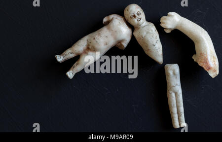 Creepy retro broken doll face and body parts isolated on grunge black background