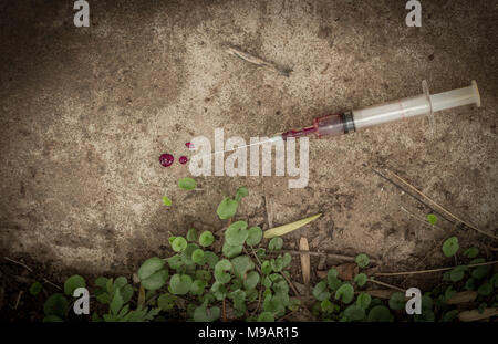 Syringe and needle with blood outdoors on pavement - Conceptual image Stock Photo