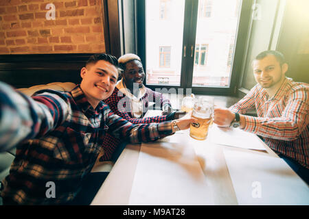 people, leisure, friendship, technology and bachelor party concept - happy male friends taking selfie and drinking beer at bar or pub Stock Photo