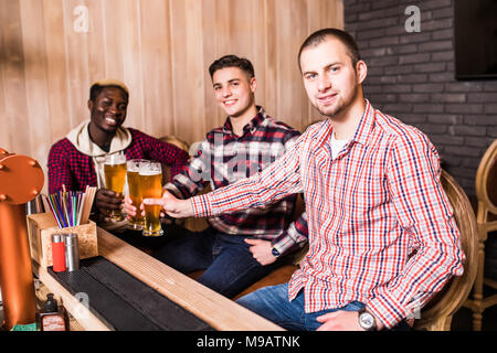 Cheerful old friends having fun and drinking draft beer at bar counter in pub. Stock Photo