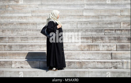 Middle age muslim woman wearing hijab standing on stairs of historical mosque called 'Yeni Cami' in Istanbul. Stock Photo