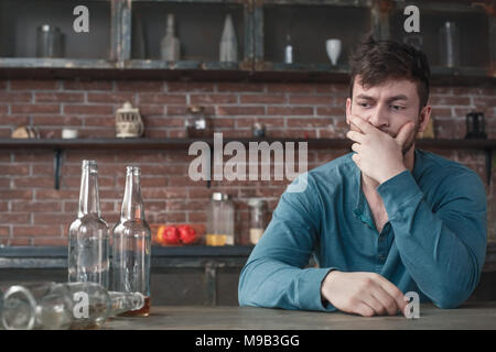 Young man alcohol addiction problems sitting at table looking at empty beer bottles thinking of problem Stock Photo