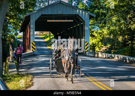 Paradise, PA - October 9, 2016: Tourists snap a picture of an Amish buggy as it exits a covered bridge in Lancaster County. Stock Photo