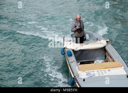 Man using mobile phone while steering boat on Rio Novo canal, Venice Stock Photo