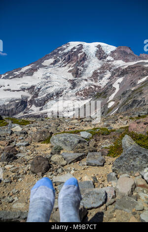 After a steep climb to edge of glacier and snow on Mount Rainier, a hiker sat down and removed hiking boots to rest feet Stock Photo