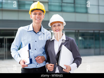 Portrait of smiling architectors who standing with folder and laptop near the building. Stock Photo