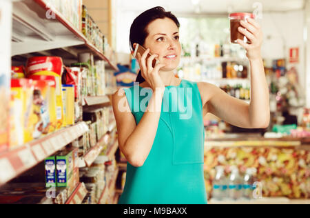 Female choosing chocolate paste and talking on the phone in the supermarket Stock Photo
