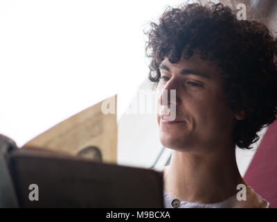 Man with Curly Hair Reading a Book Before the Window Stock Photo