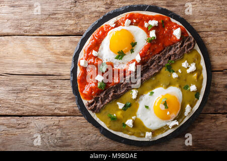 Mexican breakfast: eggs huevos divorciados with beans Frijoles refritos, two sauces roja and verde and cheese Queso Fresco close-up on the table. hori Stock Photo