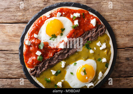 Mexican fried huevos divorciados eggs with salsa verde and roja, cheese, black beans on a tortilla close-up on a table. horizontal top view from above Stock Photo