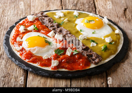 Mexican fried huevos divorciados eggs with salsa verde and roja, cheese, black beans on a tortilla close-up on a table. horizontal Stock Photo