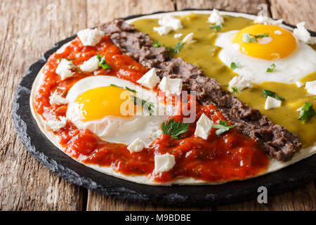 Home Mexican food: huevos divorciados with Frijoles refritos, two sauces roja and verde and cheese Queso Fresco on a corn tortilla macro. Horzontal Stock Photo