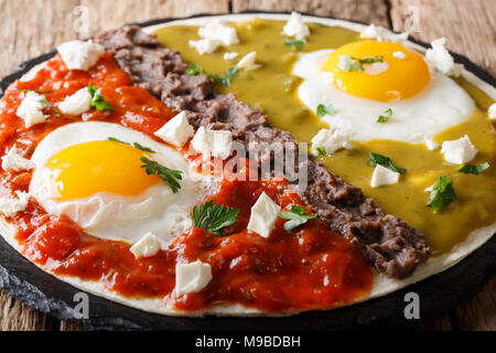 Delicious mexican dish: eggs huevos divorciados with Frijoles refritos, two sauces roja and verde and cheese Queso Fresco on a corn tortilla macro. Ho Stock Photo