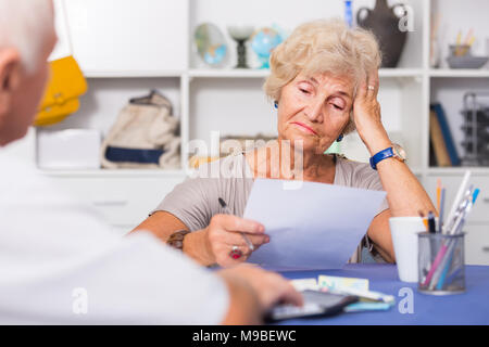 Upset senior woman sitting at home table discussing with husband their bills Stock Photo