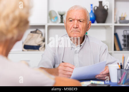 Upset senior man sitting at home table discussing with wife their bills Stock Photo