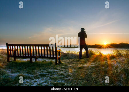 Man birdwatching at dawn Southport, Merseyside. UK Weather.  March, 2018  Cold colourful sunrise over Marshside Nature Reserve as a photographer takes pictures of avian wildlife.  Early patches of mist and fog but a mainly dry and fine day today with spells of sunshine. Stock Photo