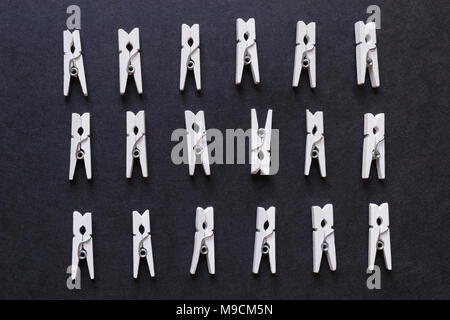 White laundry pins on black surface background. One of the pins watching head down Stock Photo