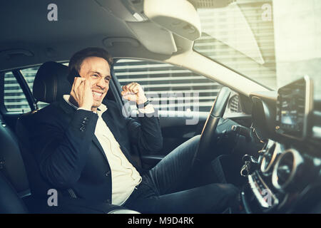 Young businessman in a blazer driving his car through they city during his morning commute celebrating success with a fist pump Stock Photo