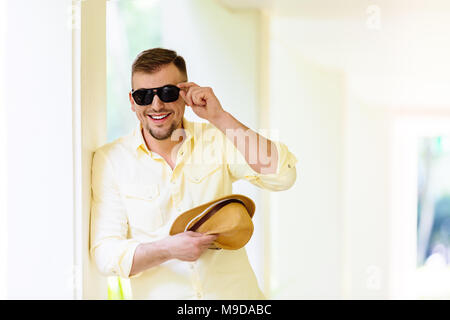 Young man in sunglasses wearing yellow hat and casual clothes having fun in sunny day. Tropical background. Stock Photo