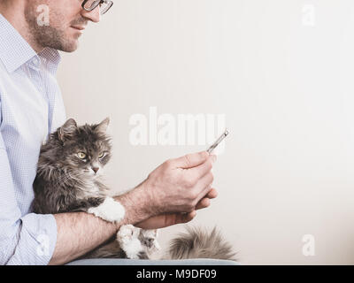 Cute man in glasses with a mobile phone on a white background holding a cute kitten. People, pets, care Stock Photo