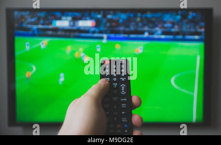Male hand holding TV remote control. Football game. Stock Photo