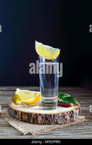 Vodka or tequila in shot glasses and in the bottle with lemon sliсe on rustic wooden background. Traditional strong drink. Close-up. Vertical view Stock Photo