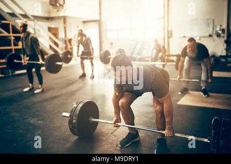 Focused young man in sportswear preparing to lift weights while working out in a gym Stock Photo