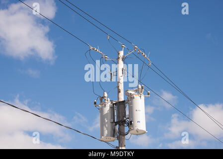 Two electric power transformers on a pole with wires, connectors and insulators with a deep blue sky and white cloud background. Stock Photo