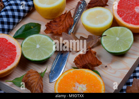 Citrus. Orange lime lemon and grapefruit cut in half placed on top of wood with leaves and an old knife. Stock Photo