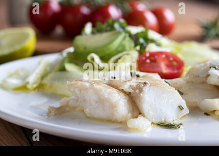 Baked cod fish with vegetable salad in the background Stock Photo