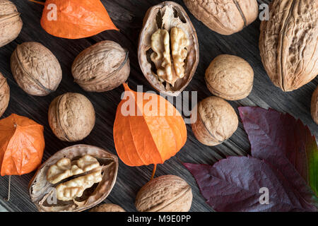Whole and broken walnuts, Physalis alkekengi (Chinese lantern) and autumn leaves on a wooden table, top view Stock Photo
