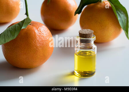 A transparent bottle of tangerine essential oil with fresh tangerines on white background Stock Photo