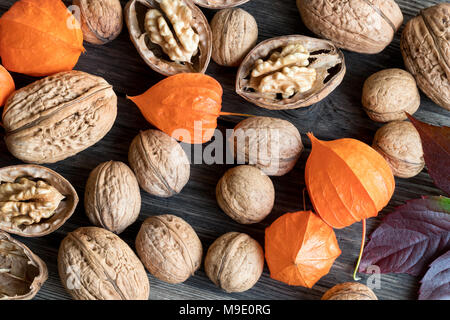 Whole and broken walnuts, Physalis alkekengi (Chinese lantern) and autumn leaves on a wooden background, top view Stock Photo