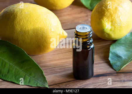 A dark bottle of lemon essential oil on a wooden table, with whole lemons in the background Stock Photo