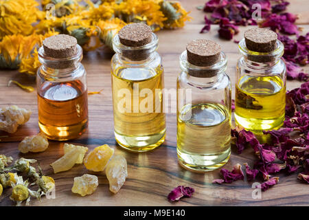 Bottles of essential oil with dried rose petals, chamomile, calendula and frankincense on a wooden table Stock Photo