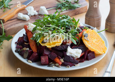 Vegetable salad - baked red beets and carrots, fresh oranges and arugula, goat cheese, roasted pumpkin and sunflower seeds. Stock Photo