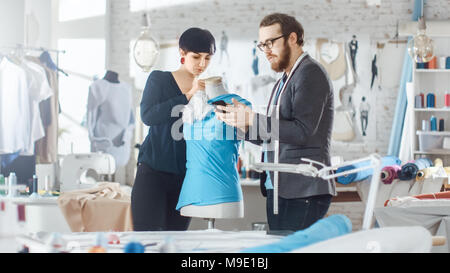 Male and Female fashion, designer, s are Working on Tailored Mannequin Wearing Clothes. They Also Use Smartphone. In Their Studio Sewing Machine Stock Photo