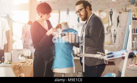 Male and Female fashion, designer, s are Working on Tailored Mannequin Wearing Clothes. They Also Use Smartphone. In Their Studio Sewing Machine Stock Photo