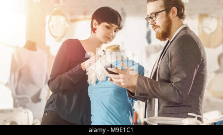 Male and Female fashion, designer, s are Working on Tailored Mannequin Wearing Clothes. They Consult Smartphone. In Their Studio Sewing Machine Stock Photo