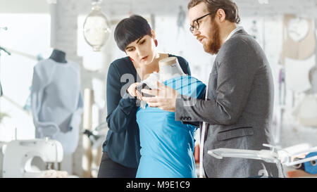 Male and Female fashion, designer, s are Working on Tailored Mannequin Wearing Clothes. They Consult Smartphone. In Their Studio Sewing Machine Stock Photo