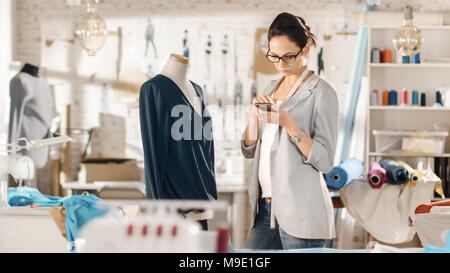 Beautiful Woman fashion, designer,  Working with Tailoring Mannequin, Adjusting Blouse, Using Smartphone. Her Studio is Bright and Sunny, Clothes Stock Photo