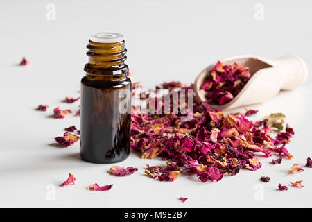 A dark bottle of rose essential oil with dried rose petals on a white background Stock Photo