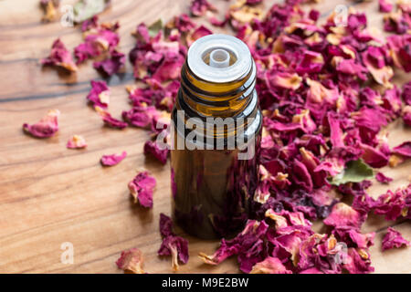 A dark bottle of rose essential oil with dried rose petals on a wooden background Stock Photo