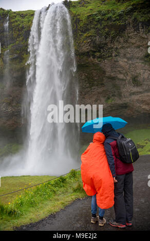 Couple admiring Seljalandsfoss waterfall on a rainy day. Seljalandsfoss. Iceland. Stock Photo