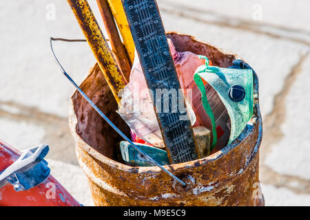 Old, grunge corroded rough metal bucket with some building tools and a construction rooler inside Stock Photo