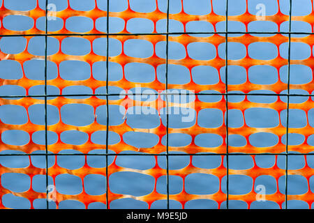 Metal wire and orange plastic mesh screen against smooth grey background. Contrast of colors Stock Photo