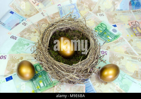 Golden egg in a nest  and two other golden eggs laying on a bed of money. Stock Photo