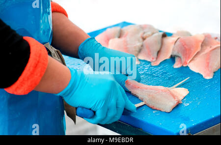 Man wearing blue gloves filleting fish with knife in close up view Stock Photo