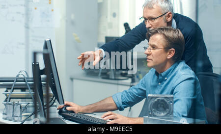 In Busy Engineering Bureau Two Senior Engineers Discussing Technical Issues over Personal Computer. Their Office Looks Minimalistic and Modern. Stock Photo